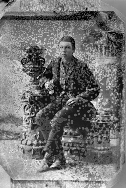 Copy photograph of a studio portrait of a Ho-Chunk boy posed sitting on a prop stone wall wearing a suit. The original is probably not taken by Van Schaick.