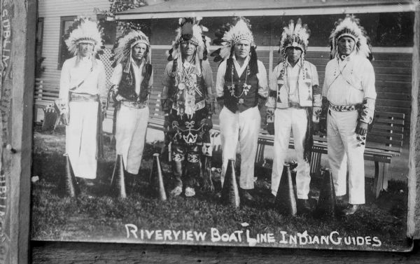 Copy photograph of six Native American men standing outdoors wearing Sioux bonnets, and original print inscribed "Riverview Boat Line Indian Guides." Possibly from the Wisconsin Dells.