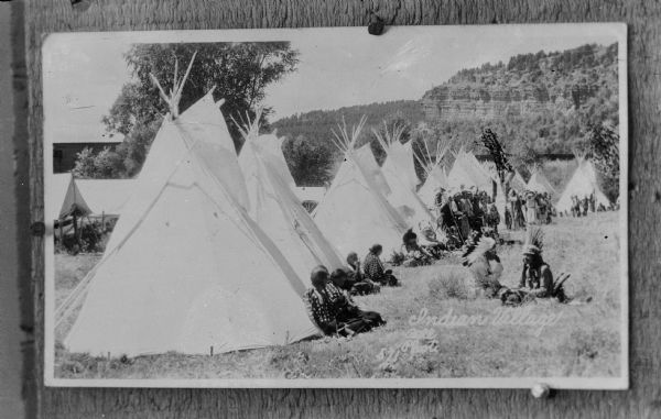 Copy photograph of a Native American/Sioux camp including a large group of people, tipis, and a long lodge. The photograph is inscribed, "Indian Village Bell Photo 571. "