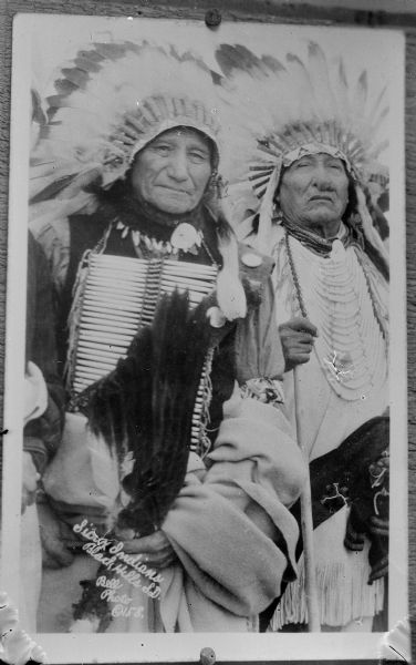Copy photograph of two Native American/Sioux men wearing full regalia, including breast plates and feathered bonnets. The photograph is inscribed, "Sioux Indians, Black Hills, S.D. Bell Photo (c) 158."