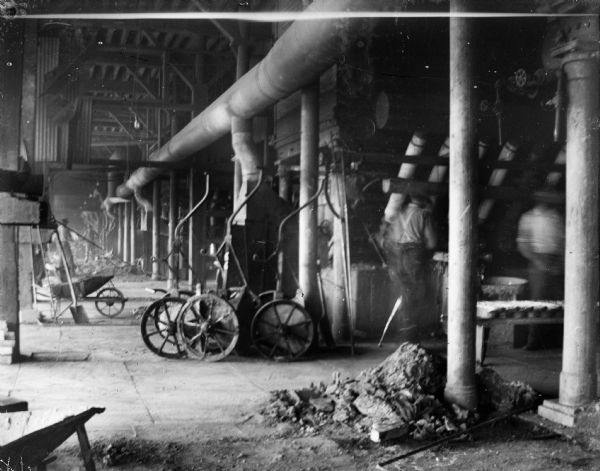 Interior of a factory with two blurred men on the right, and men in the background on the left.