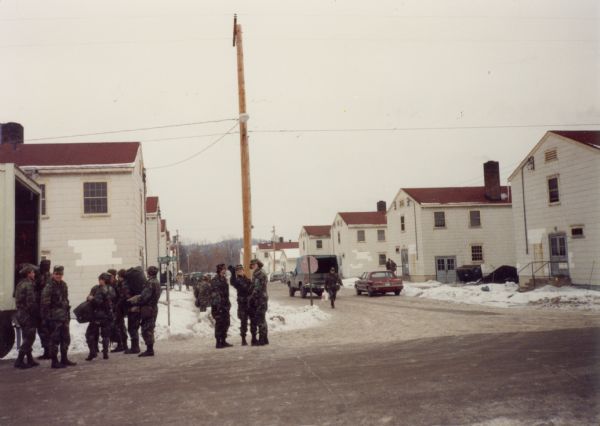 Fort McCoy, showing housing, and soldiers standing at the back of a truck at wintertime.