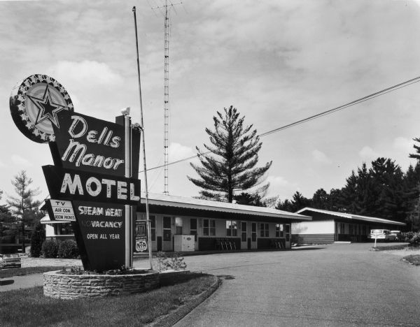 Front of Dells Manor Motel, with parking lot and neon sign.