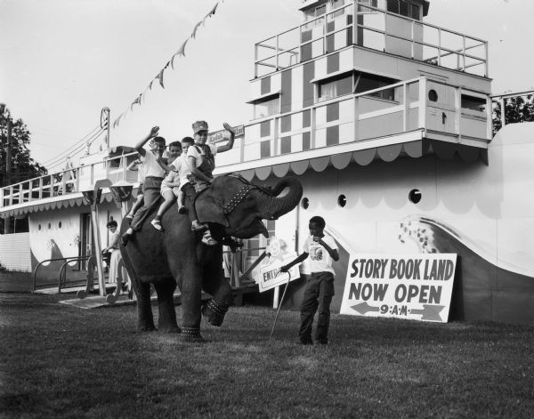 Six children ride an elephant in front of boat-shaped entrance to Story Book Land.