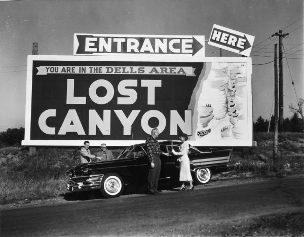 Sign for Lost Canyon, with people standing near a car in the foreground.