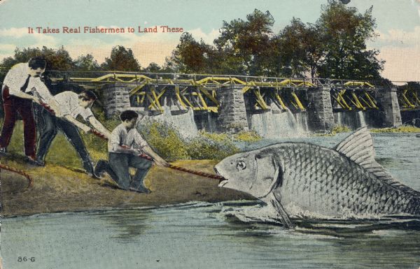 Three men attempt to pull a giant fish onto shore using a rope. A dam spans the length of the river in the background. Red text in the upper left corner bears the text, "It Takes Real Fishermen to Land These."