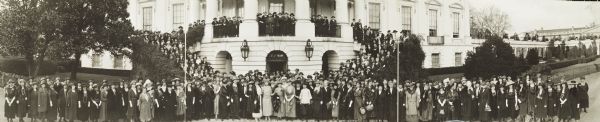 Panoramic view of the 36th annual general meeting of the Association of Collegiate Alumnae reception at the White House. There is a crowd of women, most wearing dresses and hats, gathered on and around the White House.