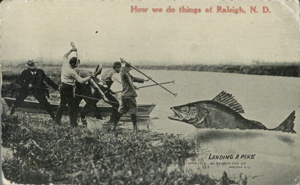 A group of men on a lakeshore grapple with a giant pike. Two men pull on a rope hooked to the pike while two more stand ready with harpoon-like sticks. Another man pours out a bottle of water on his head. Red text in the upper portion of the image reads, "How we do things at Raleigh, N.D."