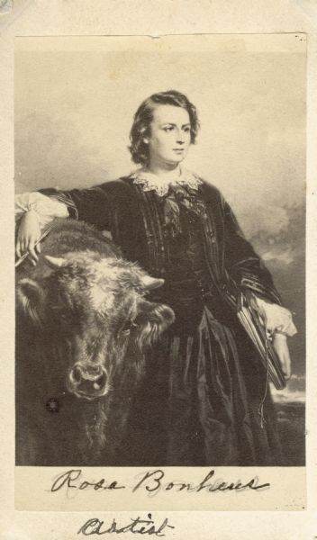 Carte-de-visite portrait, reproduced from a painting by Louis-Edouard Debufe, depicting French Artist Rosa Bonheur (1822-1899). This painting depicts the artist with a cow, symbolic of her work as a painter of animals. The feminine attire in this portrait is misleading, however, as she was known for wearing men's clothing. Handwritten inscription at bottom reads, "Rosa Bonheur, Artist."