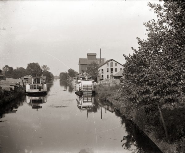 Steamboats docked in the Portage Canal, which was hand dug beginning in 1849 and completed in 1851. There are industrial buildings on either side of the canal in the background.