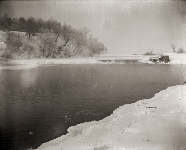 Fox River during the winter. A hill with trees on the far shoreline can be seen in the background.