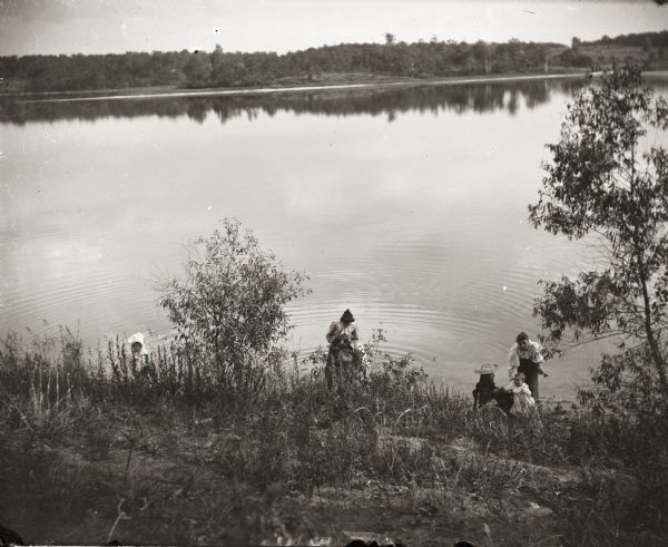 View down hill of group of women and children on the shore of Birch lake.