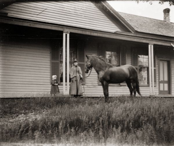 Ada Bass and her daughter Everetta standing on the front porch of their home. Ada is holding onto the reins of a horse named Niger.