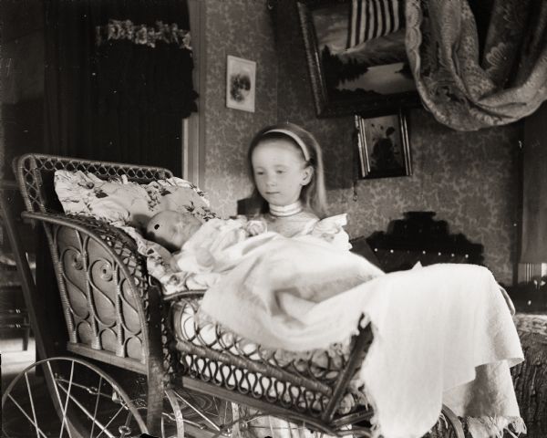 Everetta Bass standing next to her brother Cary, asleep in a baby carriage. They are most likely inside the Bass family home.