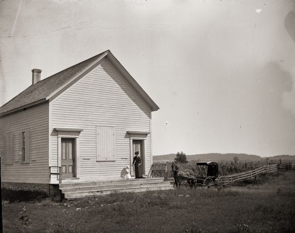 Woman and child standing on the steps of the Avery School House. A horse and carriage stand nearby.