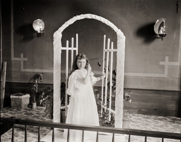 Girl (probably Everetta Bass, the photographer's daughter), opening a decorative gate. She is posed inside a local church.  The Bass family attended the Methodist church.