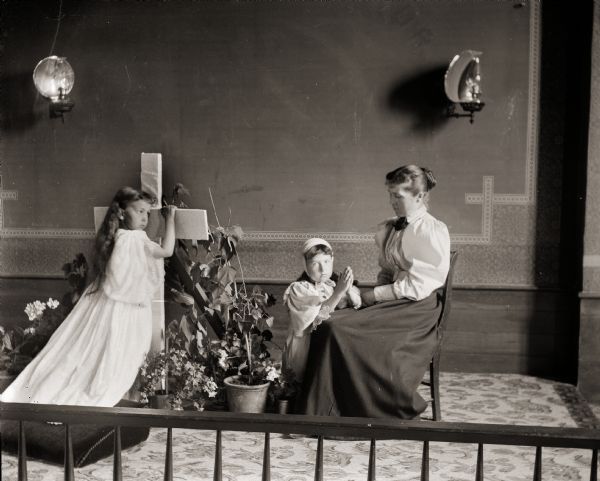 A woman, identified as Mrs. Blore, is seated with two girls in a Montello church. The young girl at the cross could possibly be the photographer's daughter, Everetta Bass.