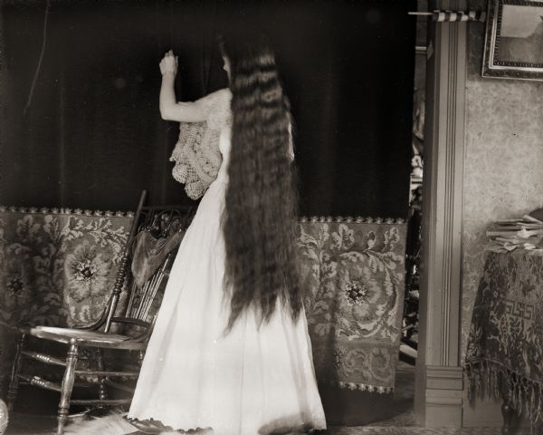 Ada Bass, wife of the photographer, standing in a room showing her long hair extending down her back.