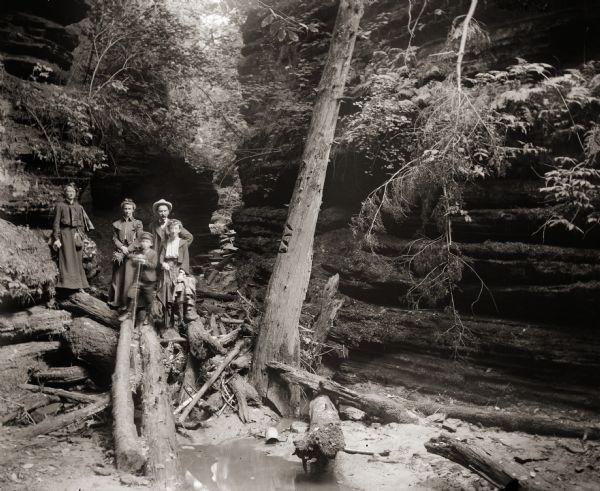 Two unidentified adults behind Cary Bass, holding a cane and standing next to his sister Everetta Bass. Their mother, Ada Bass stands apart on the left. They are in a gorge at the Wisconsin Dells.