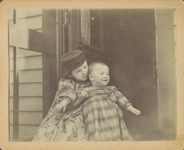 Everetta Bass holds her brother, Cary (Edward C.) Bass in a doorway.  On the reverse, in Dr. Bass's handwriting, "Here is a pugilistic grin for you, on the face of this boy."