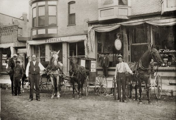 Three rural mail carriers pose with their horses and buggies in front of the Montello Post Office.  Postmaster (Dr.) Edward A. Bass stands in the background against the building.  Frank Shannon's jewelry business shared the storefront with the post office.