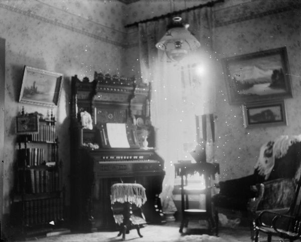 The parlor in the home of Dr. Edward Bass showing a parlor organ near a window, and other furnishings.