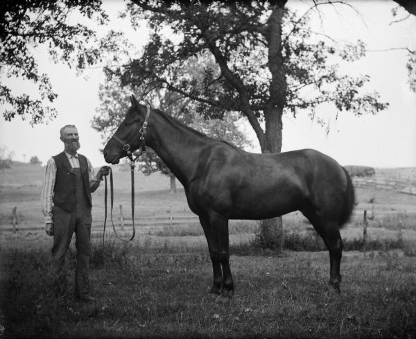 Leroy J. Burlingame, the photographer's father-in-law, and his horse Dan standing outdoors near trees.