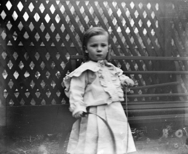 The photographer's son, Edward Cary Bass, with a hoop. There is a lattice fence behind him.
