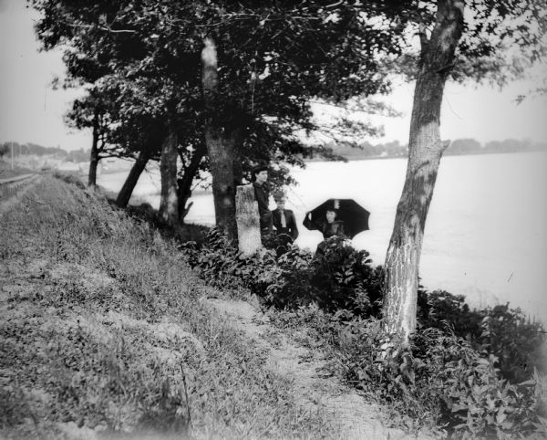 Three unidentified women with umbrellas on the north shore of Buffalo Lake. Buildings of Montello are visible in the background.