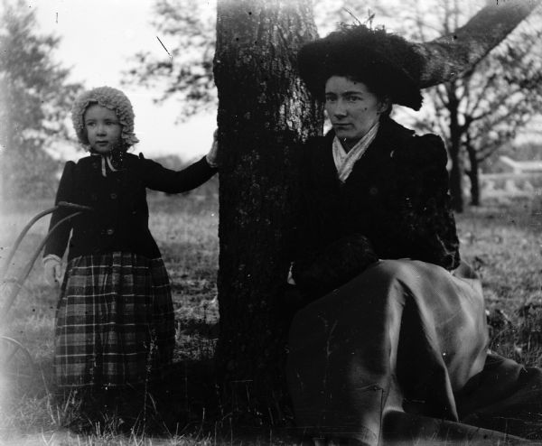 Ada Bass and her daughter Everetta near a tree on Court House Hill. The handle of a toy baby buggy is on the left.