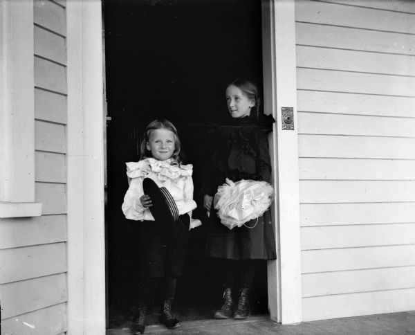 The photographer's children, Cary and Everetta Bass, standing in an open doorway. They are each holding a hat.