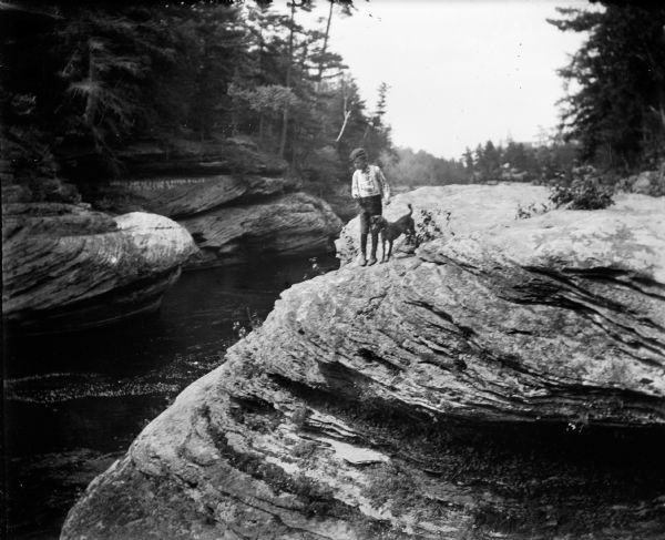 The photographer's son, Cary Bass, and a dog on a rock formation in the Wisconsin Dells near the Wisconsin River. In the background there is writing on a rock, that says "Leroy Gates  Dells River Pilot  1849 to 1858."