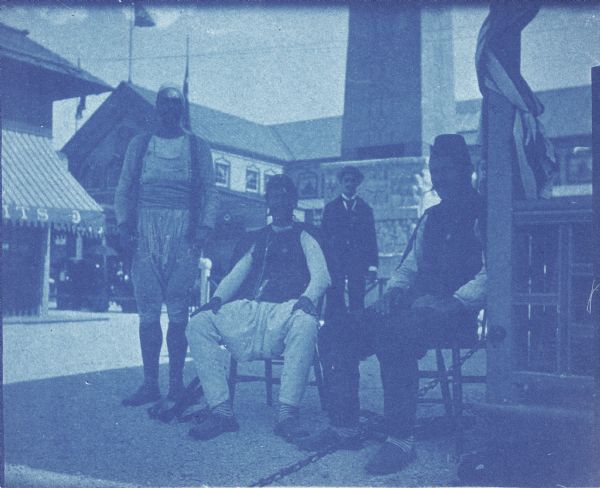 Three men in Arab dress pose in front of the base of an obelisk on the Midway at the World's Columbian Exposition. A gentleman in western dress also poses in the background.