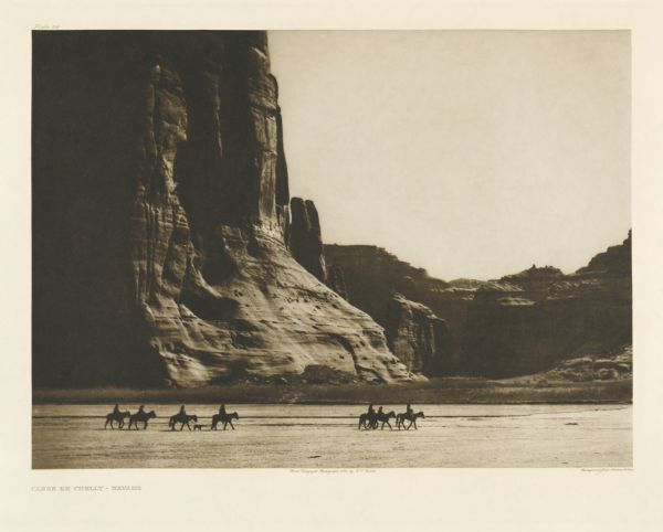 The original caption reads: "A wonderfully scenic spot is this in northeastern Arizona, in the heart of the Navaho country — one of their strongholds, in fact. Canon de Chelly exhibits evidence of having been occupied by a considerable number of people in former times, as in every niche at every side are seen the cliff-perched ruins of former villages." A view of riders on horseback in the Canon de Chelly.