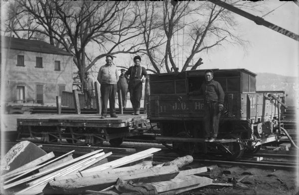Group of men standing on and beside a rail car in front of the main construction office at the site of the Wisconsin River dam.