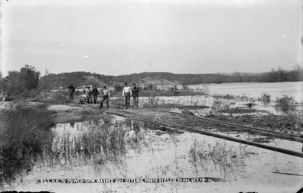 Workmen standing on damaged and partly submerged railroad track on the west shore of the Wisconsin River.