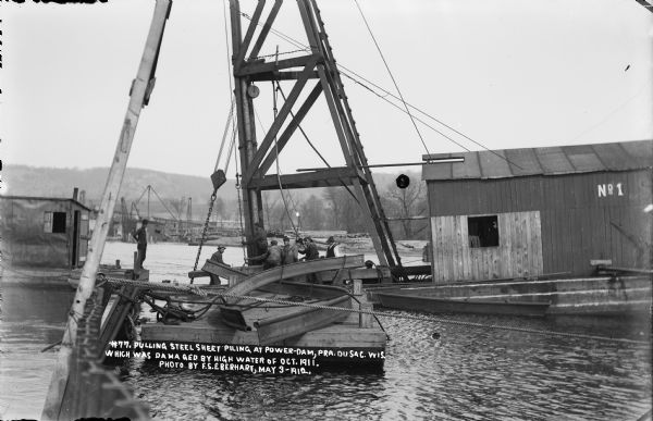 Workmen on a barge using a pulley to raise sheet steel pilings which were damaged by high water in October, 1911.