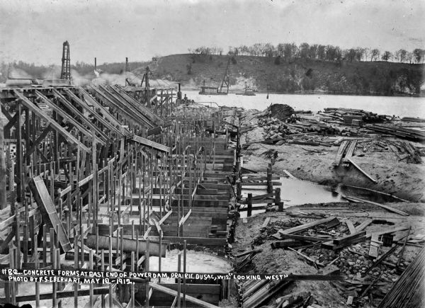 Work progresses on the wooden concrete forms at the east side of the river. The steam-powered pile drivers are also visible.