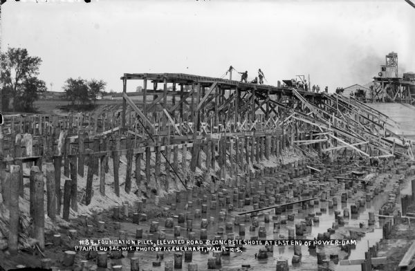 Men working from the elevated road on the east end of the power dam, constructing shots (chutes) for the concrete.