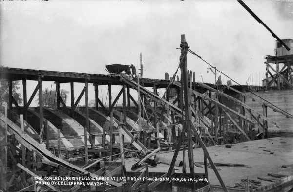 Forms have been removed, revealing the newly poured buttresses and apron. A man is pushing a cart on the elevated road.