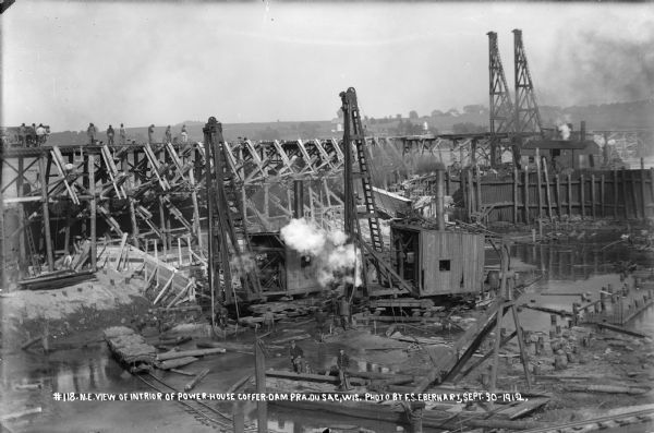 Pile drivers working within the confines of the coffer dam. Men are on the high trestle constructing chutes for pouring concrete.