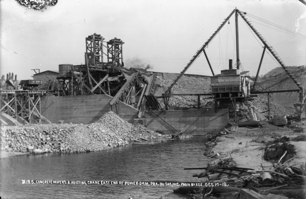 Concrete plant at east end of the dam, showing the mixers, crane, and a rail car at the abutment.