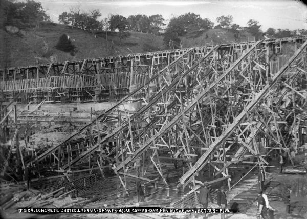 Men working on the concrete chutes and elevated trestle. Iron reinforcing bars protrude from the forms.