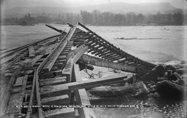 A view, looking east, of the wreckage of the high trestle caused by flooding and ice. The concrete plant is visible on the far bank.