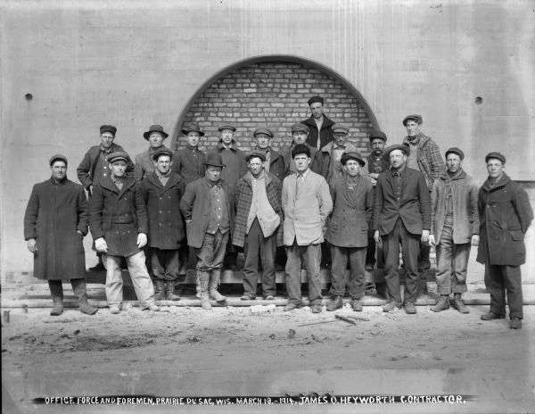 The office force and foremen posing before the south facade of the power house at the Prairie du Sac dam.