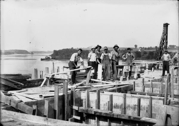A group of workmen posing while working on concrete forms at the Prairie du Sac dam site. Their position high above the water level affords an expansive upstream view of the Wisconsin River.