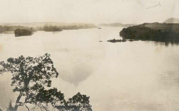 Elevated view of high water on the Wisconsin River from a bluff on the west bank. The photograph is undated and does not indicate if it was taken prior to the construction of the dam at Prairie du Sac. Caption reads: "View North of Pounds Landing, Prairie du Sac, Wis."