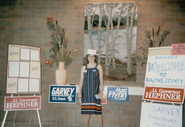 A woman stands near a sign welcoming Democrats to Racine County. Political signs say: "Lt. Governor Hephner," "Garvey U.S. Senate," and Matt Flynn U.S. Senate."
