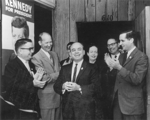 Wisconsin State Senator, Horace Wilkie, center, is applauded after cutting a ribbon to open the new Madison joint headquarter of the Citizens for Kennedy and the Nelson for Governor committees.  The office is located at 610 University Avenue.  Looking on, left to right:  Patrick Lucey, state Democratic chairman; Madison Mayor Ivan Nestingen, state co-chairman of the Citizens for Kennedy committee; Wilkie; Don Eisenberg, Dane County chairman of the Kennedy-Johnson volunteers; Mrs. Robert Dolan, a volunteer worker; Jack DeWitt, Dane County chairman of Citizens for Kennedy; and Pat Kennedy, a UW graduate student from New York (no relation to the candidate) also a volunteer worker.