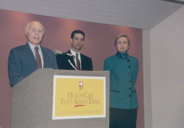 Senator Herbert H. Kohl, Russ Feingold, and Hillary Clinton. Sign on podium says "Health Care That's Always There, The National Health Care Campaign".